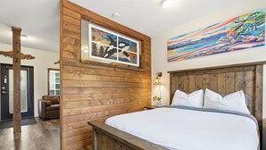 A bedroom with a wooden headboard, a bed with white bedding, a painting above the bed, and a wooden wall panel. - Steps to Terrace Beach & Trails • Whale’s Tail (Ucluelet)