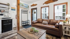 A modern kitchen with a built-in refrigerator, a dining area with a brown leather couch, and a wooden coffee table. - Steps to Terrace Beach & Trails • Whale’s Tail (Ucluelet)
