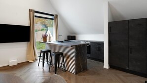A modern kitchen with a black countertop, a window with curtains, and a dark cabinet.