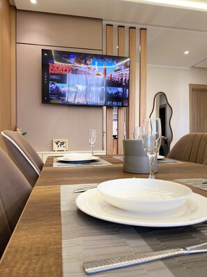 A conference room with a large flat-screen TV mounted on the wall displaying a movie. The room has a long wooden table set for a meeting, with plates, glasses, and cutlery. There are leather chairs around the table, and a framed picture on the wall. - Sunset View Apartment☀️🌴 Swimming-pool/Garden/Terrace 15M walk to the beach🏖️ (Agadir)