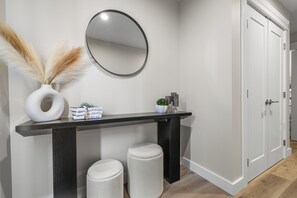 A modern hallway with a dark wooden console table, a round mirror, and two white stools.