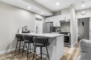A modern kitchen with a central island, bar stools, stainless steel appliances, and a clock on the wall.