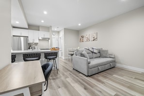A modern kitchen with white cabinets, a stainless steel refrigerator, and a dining area with a wooden table and black chairs.