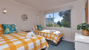 Ein Hotelzimmer mit zwei Betten, einem kleinen Schreibtisch, einem Fenster mit Blick und einem Blumentopf.