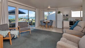 Ein modernes Wohnzimmer mit einer Couch, Sesseln, einem Esstisch und einer Küchenzeile.
