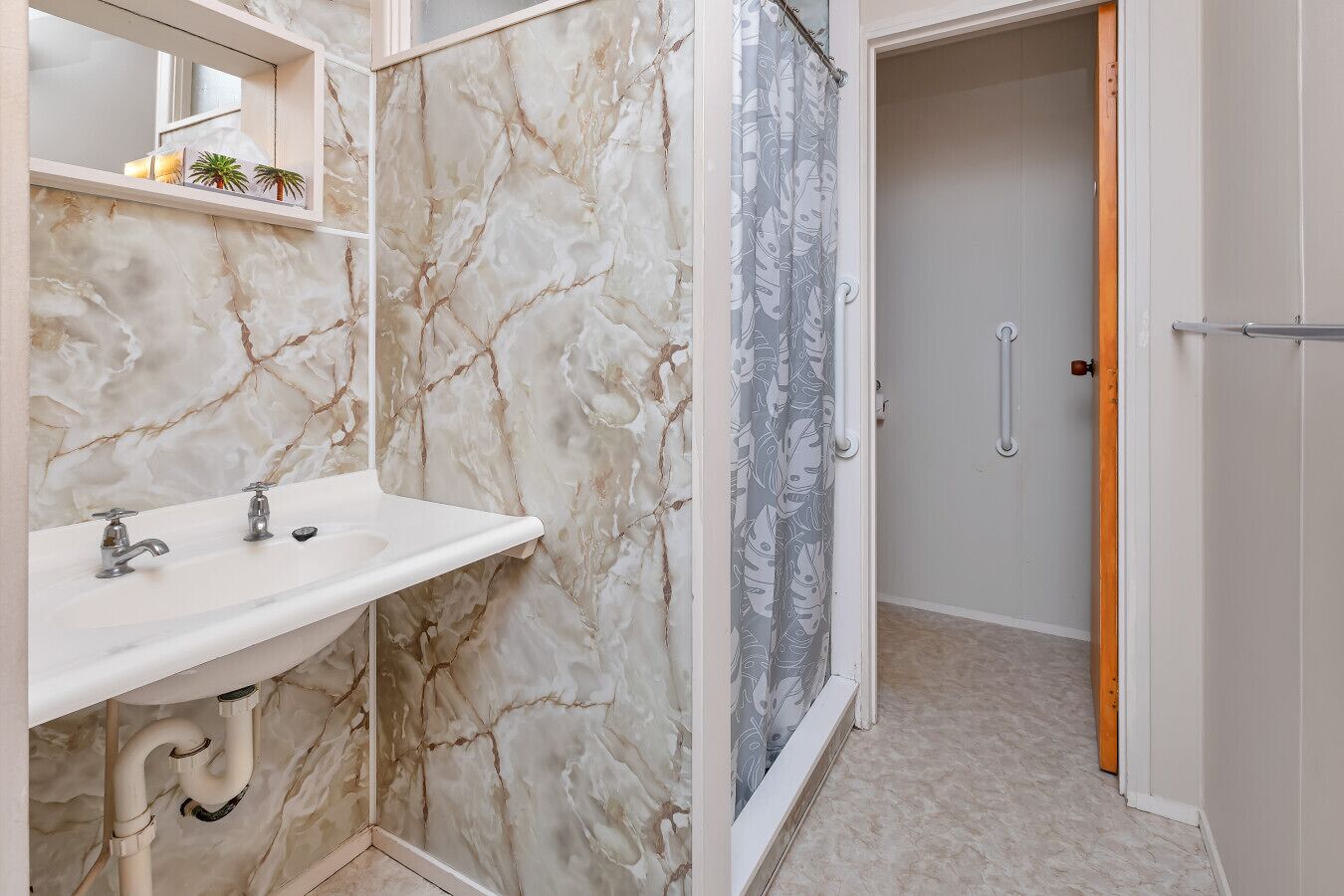 A bathroom with a marble sink, a shower with a grey curtain, and a door with a handle.