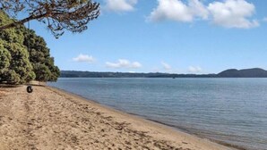 Ein Strand mit sandigem Ufer, ruhigem Wasser und sanften Hügeln im Hintergrund.