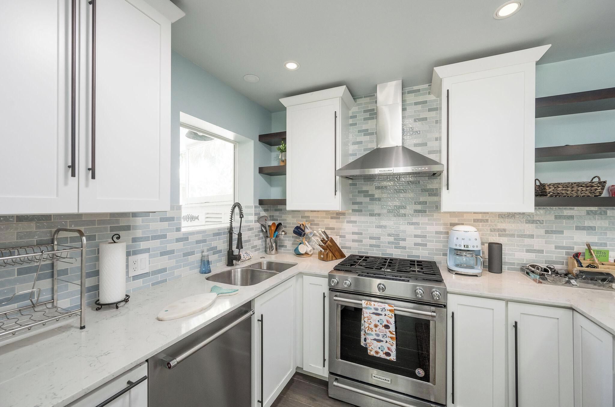 Una cocina moderna con gabinetes blancos, estufa de acero inoxidable y un revestimiento de azulejos.