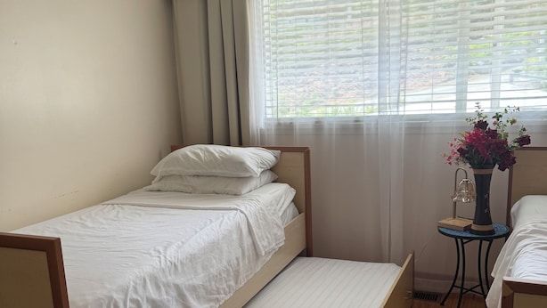 A single bed with a wooden frame, a small bedside table with a lamp, and a window with blinds.