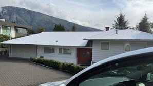 A residential house with a garage, a red door, and a snow-covered roof.