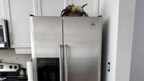 A stainless steel refrigerator with a water dispenser, a microwave, and a small oven in a kitchen with white cabinets and a tiled floor.