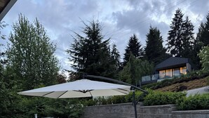 A patio area with outdoor furniture, a large umbrella, and a stone wall. - Entire Peaceful 3BR Guest Suite Upper Level West Vancouver: WiFi & Parking (West Vancouver)