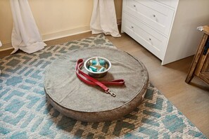Un pouf rodó amb una corretja vermella i un bol metàl·lic sobre un estotge estampat.