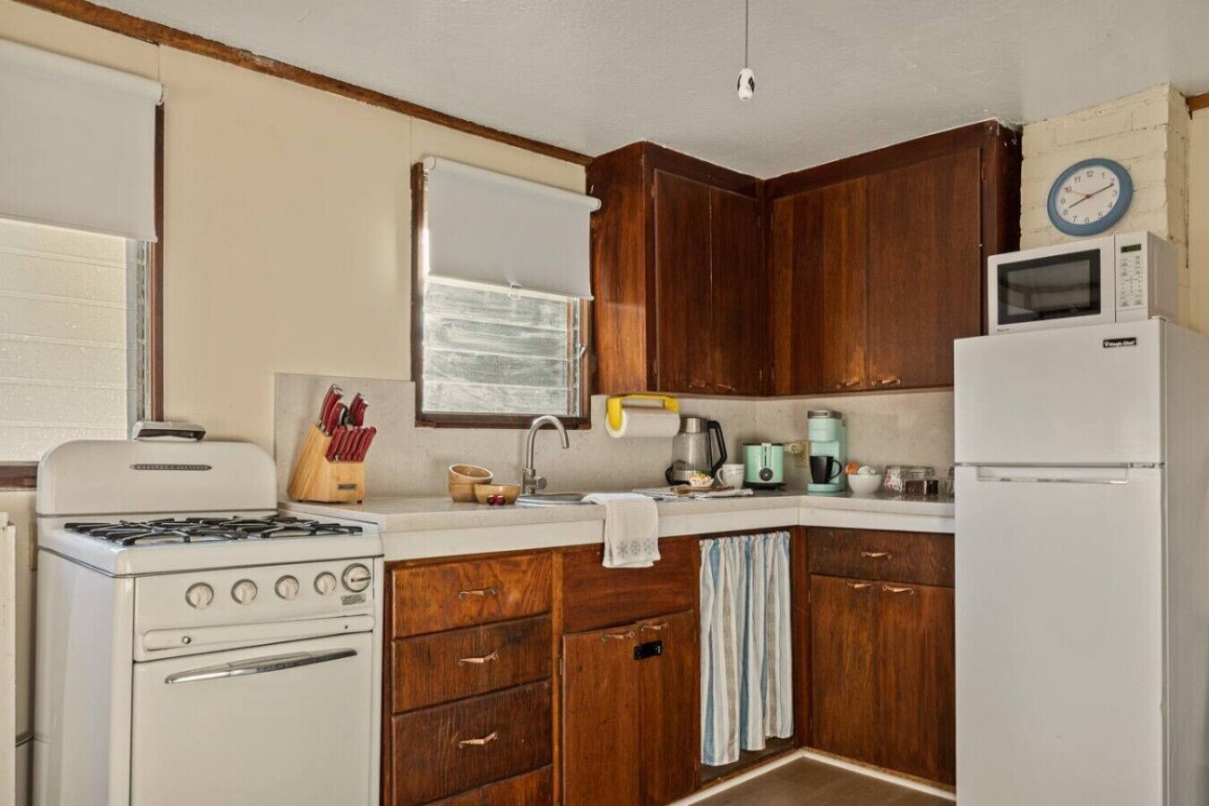 A compact kitchen with wooden cabinets, a stove, a microwave, and a refrigerator.