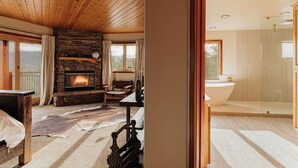 A cozy living room with a fireplace, a stone wall, and a view of the outdoors. - Cliffhanger Cabin, Near Snow Summit w/ Hot Tub (Big Bear Lake)