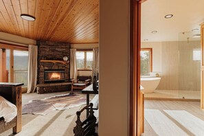 A cozy living room with a fireplace, a stone wall, and a view of the outdoors. - Cliffhanger Cabin, Near Snow Summit w/ Hot Tub (Big Bear Lake)