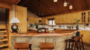 A rustic kitchen with wooden cabinets, a stone island, and hanging pendant lights. - Cliffhanger Cabin, Near Snow Summit w/ Hot Tub (Big Bear Lake)