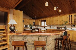 A rustic kitchen with wooden cabinets, a stone island, and hanging pendant lights. - Cliffhanger Cabin, Near Snow Summit w/ Hot Tub (Big Bear Lake)