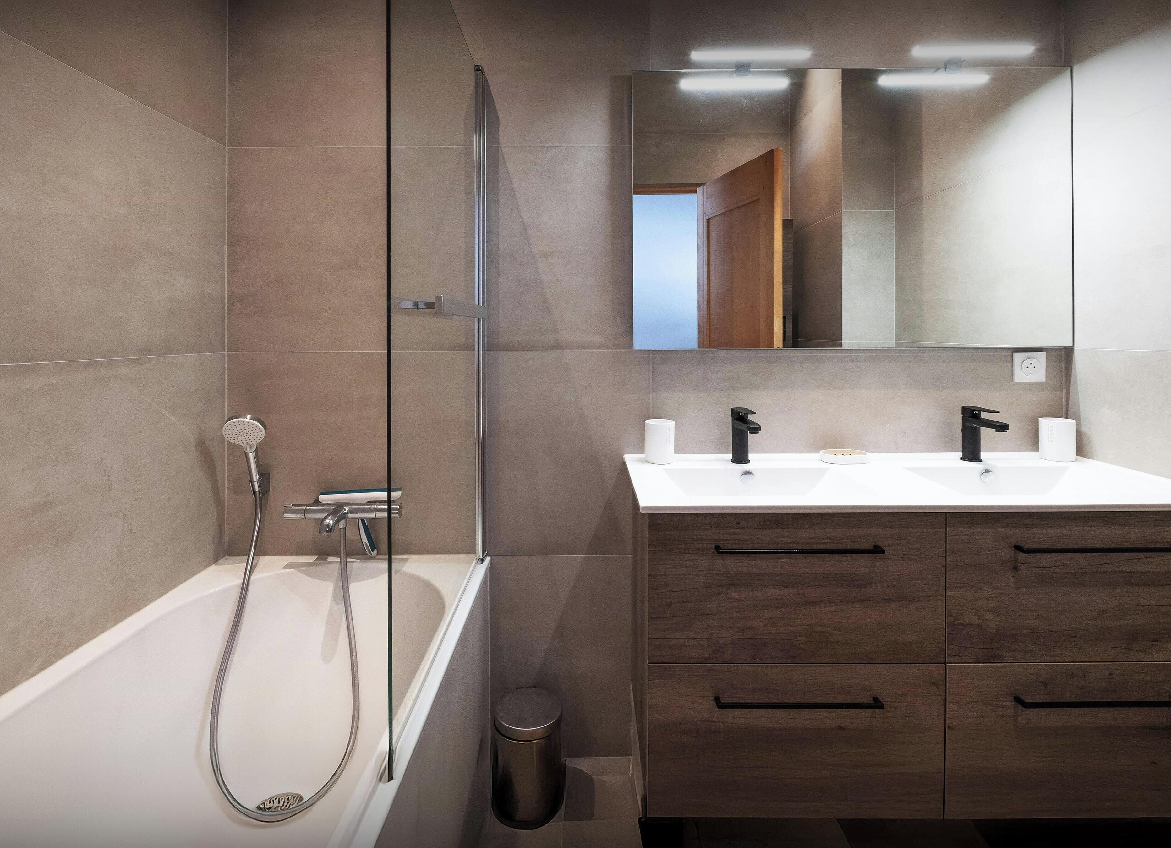Un baño moderno con bañera, dos lavamanos, un espejo y un cubo de basura.