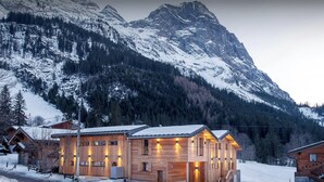 Un lodge in legno con diverse stanze, una scala e vista sulle montagne innevate.