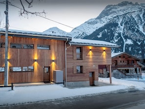 A wooden building with multiple windows and a door, set against a snowy mountain backdrop.