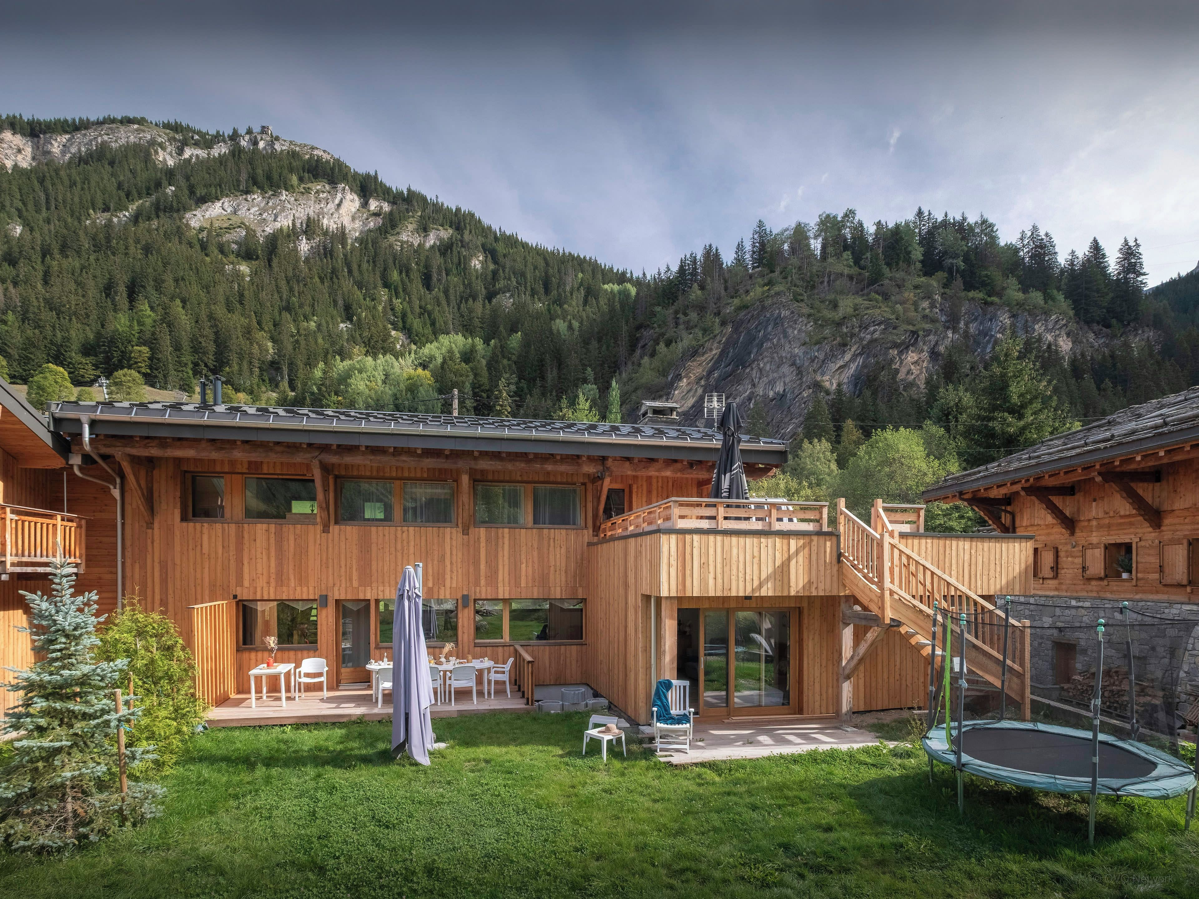 Eine Holzhütte mit Balkon, Essbereich und einem Trampolin im Garten.