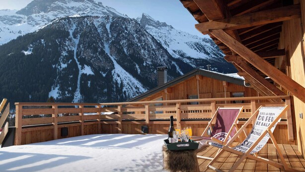 Una baita di legno con veranda in legno, una bottiglia di vino, bicchieri e un cartello in francese.