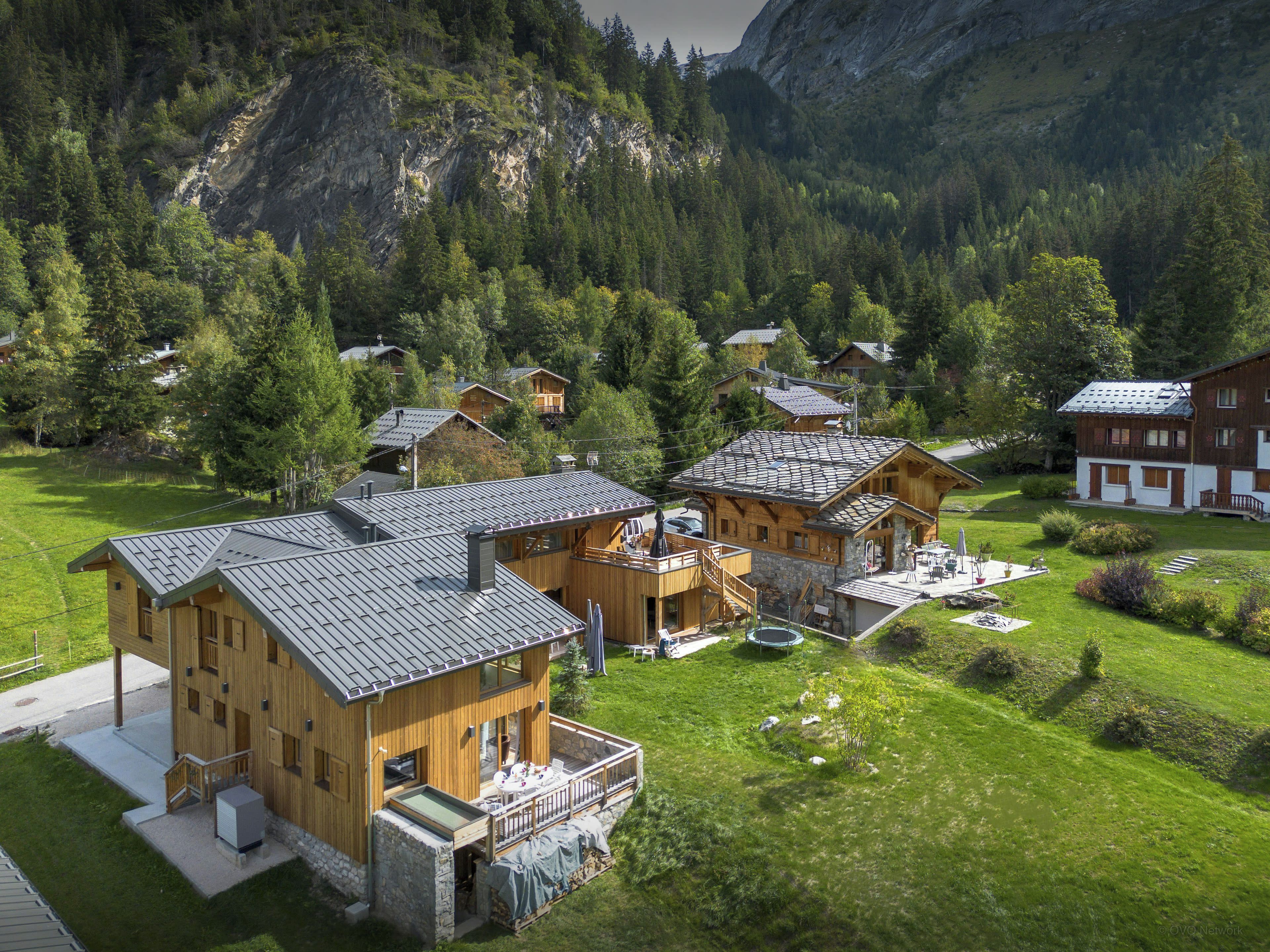 Eine Berglodge mit mehreren Holzhäusern, einem überdachten Sitzbereich im Freien und Blick auf den umliegenden Wald und die Berge.