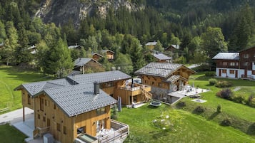 Eine Berglodge mit mehreren Holzhäusern, einem überdachten Sitzbereich im Freien und Blick auf den umliegenden Wald und die Berge.