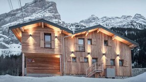A wooden cabin with a stone foundation, multiple windows, and a staircase leading to a balcony. - Chalet Arpitan Orizon - Chalet in the Vanoise National Park - OVO Network (Pralognan-la-Vanoise)