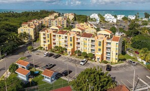 A multi-story residential building with balconies, a parking lot, and a view of the ocean.