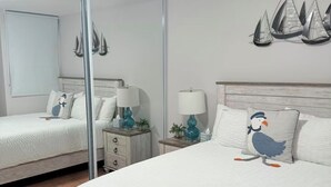 Een slaapkamer met een bed, nachtkastje, spiegel en een decoratie aan de muur.
