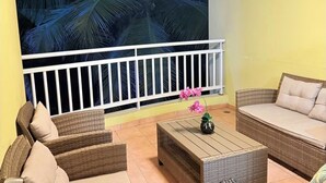 Een balkon met rieten meubels, een plafondventilator en een grote muurschildering van een tropisch blad.