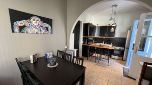 Un coin repas avec une table et des chaises en bois foncé, un tableau au mur et une cuisine en arrière-plan.