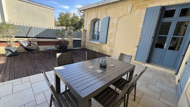 Une terrasse avec une table et des chaises, un barbecue et une porte bleue.