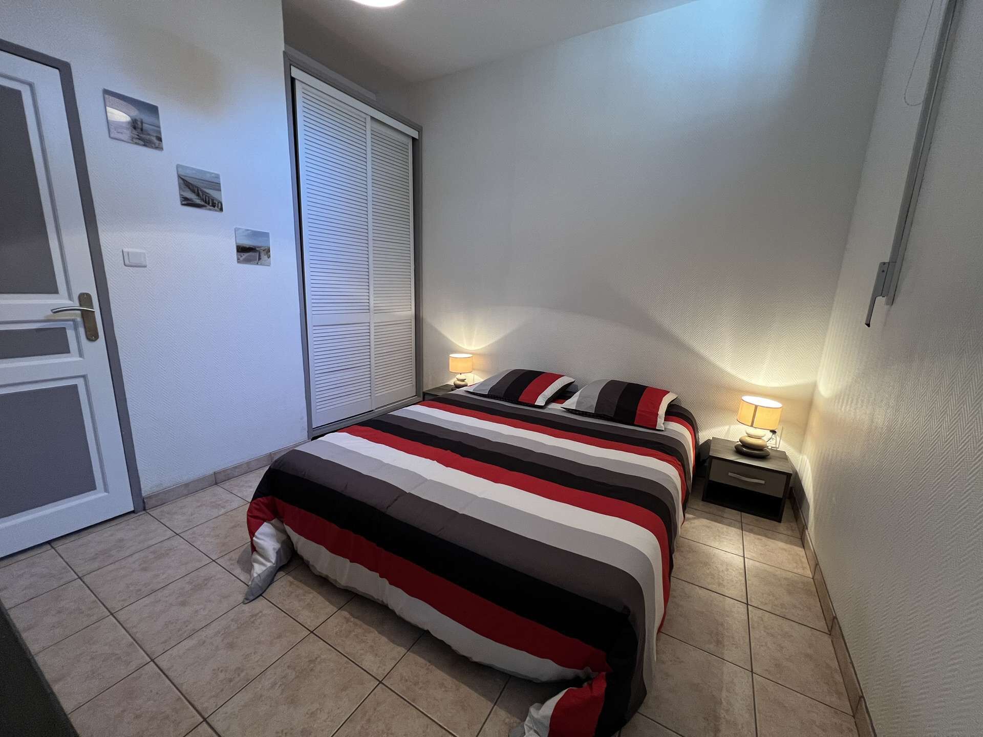 A bedroom with a bed, bedside tables, a door, and a window with blinds.