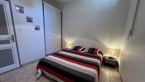 Une chambre à coucher avec un lit, des tables de chevet, une porte et une fenêtre avec des stores.