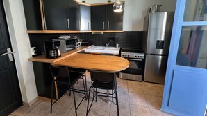 Une cuisine moderne avec des meubles de couleur noire, un plan de travail en bois, un réfrigérateur en acier inoxydable et un four encastré.