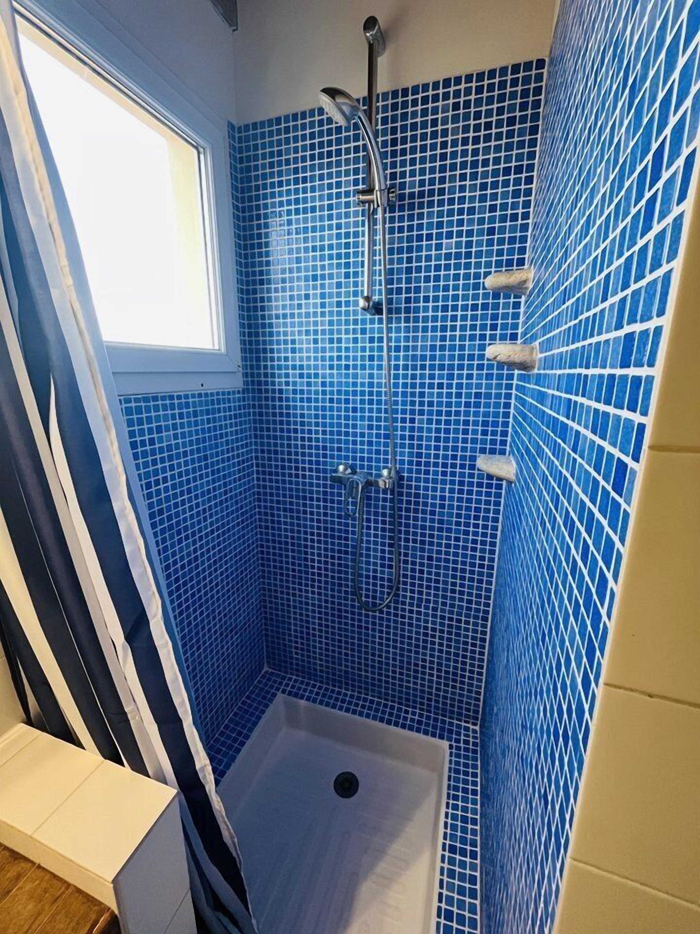 A small, enclosed shower area with blue mosaic tiles, a showerhead, and a window.