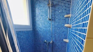Ein kleiner, abgeschlossener Duschbereich mit blauen Mosaikfliesen, einer Duschbrause und einem Fenster.