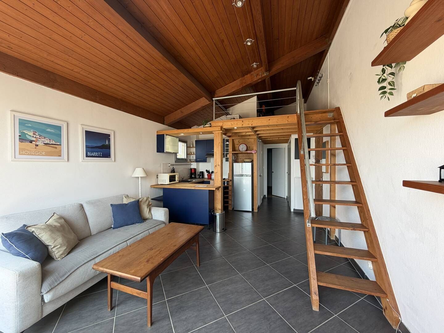 Un intérieur moderne avec un plafond en bois, un canapé, une table en bois, un coin cuisine et un escalier.