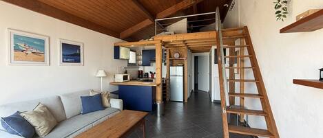 A modern interior with a wooden ceiling, a sofa, a wooden table, a kitchen area, and a staircase.