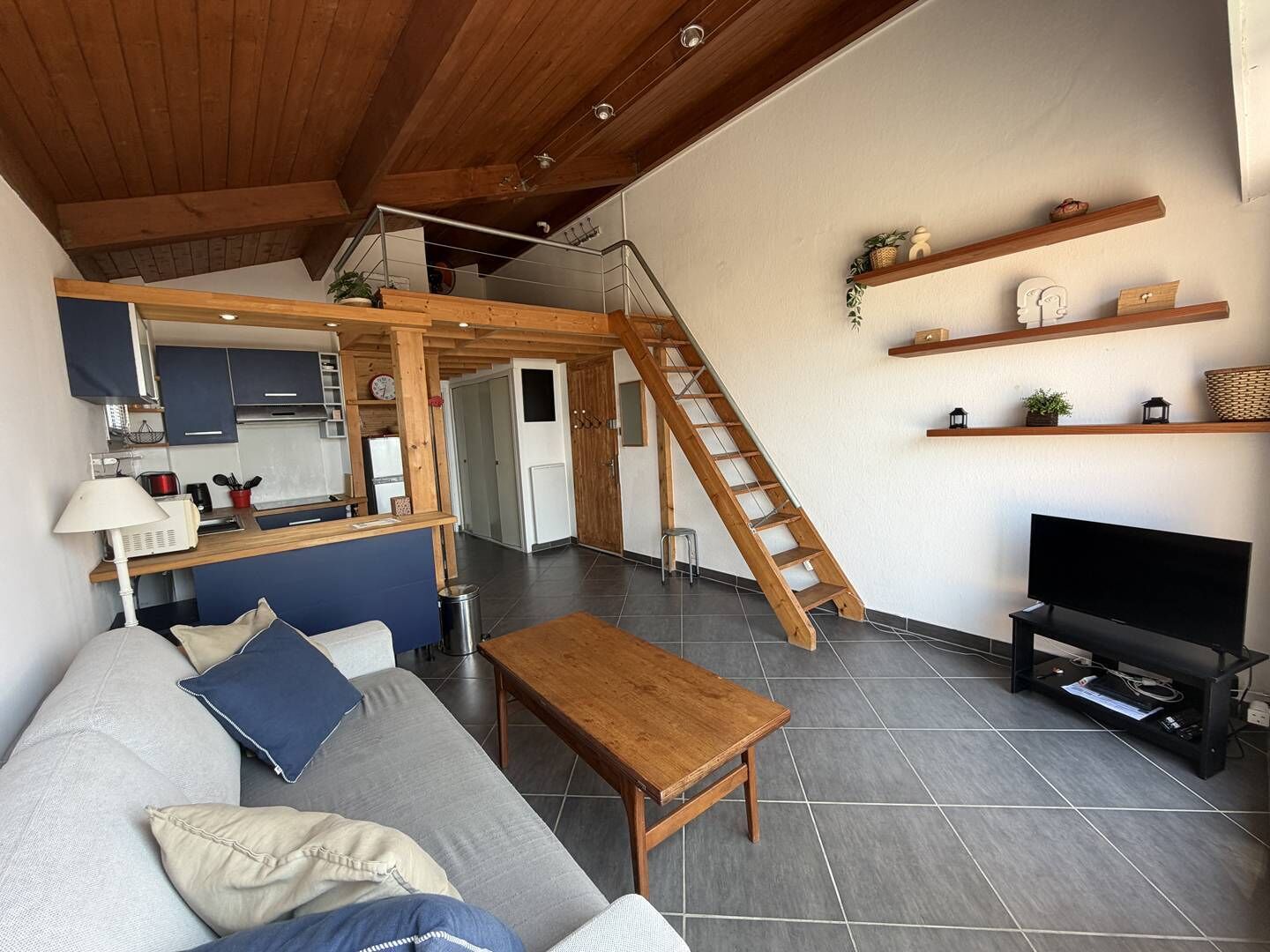 Un espacio habitable moderno con una escalera de madera, un sofá, una mesa de centro, un televisor y una zona de cocina.