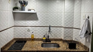 Eine Küche mit weißen Fliesenwänden, einer Granitarbeitsplatte, einem eingebauten Herd, einer Spüle und einem Regal mit Küchenutensilien.