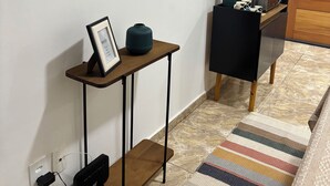 Ein modernes Wohnzimmer mit einem an der Wand befestigten Flachbildfernseher, einem Holztischchen mit Bilderrahmen und einer Vase, einem schwarzen Sessel und einem Streifenmuster-Teppich auf dem Boden.