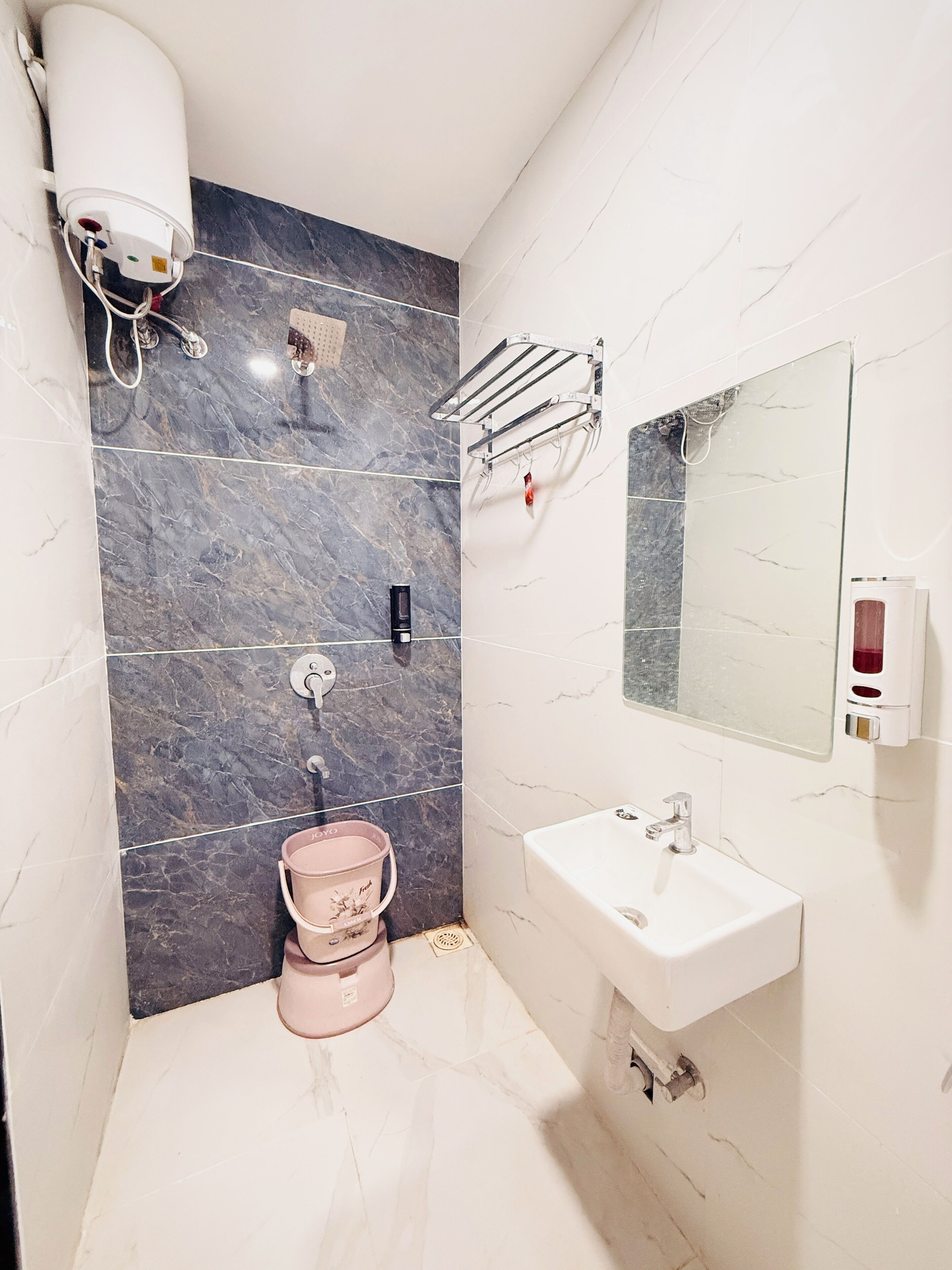 Un baño con pared de mármol, un lavamanos, un espejo, un perchero para toallas y un inodoro.