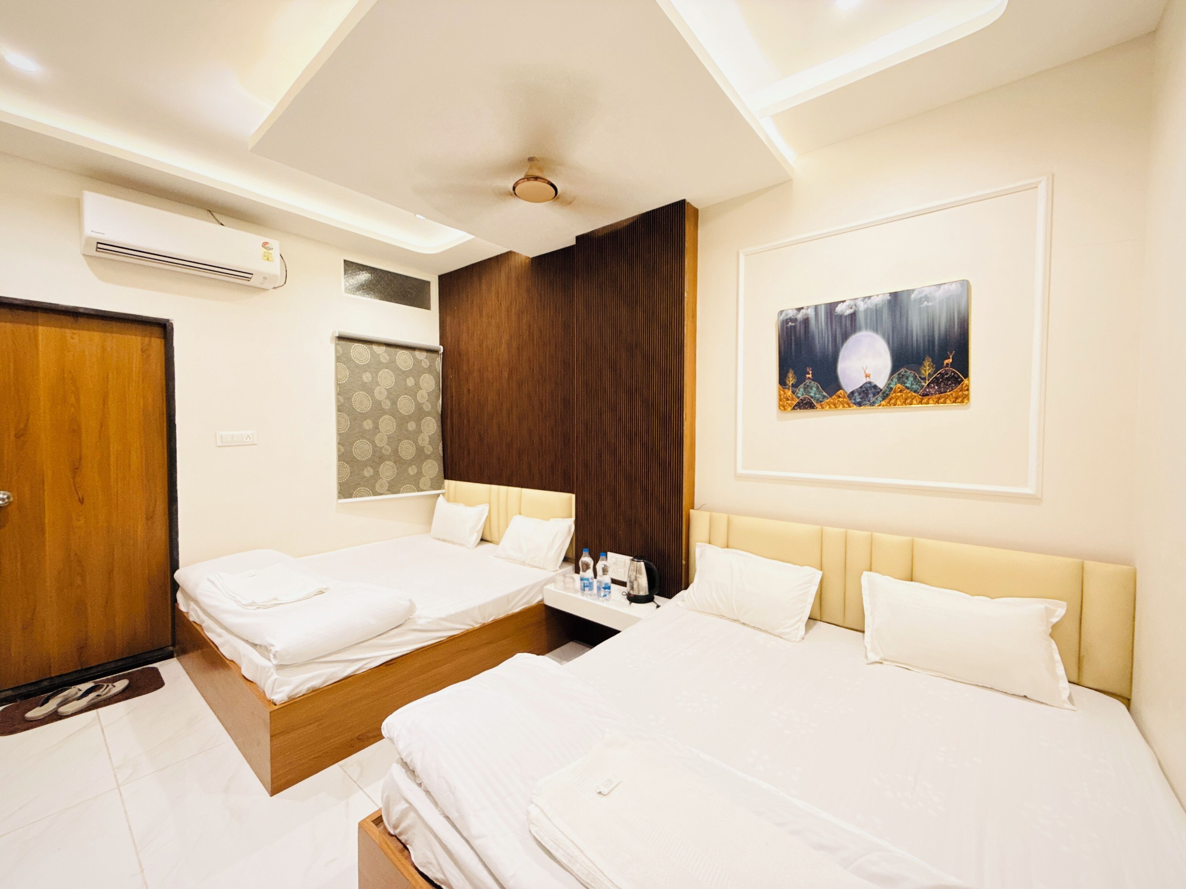 A hotel room with two beds, a ceiling fan, an air conditioning unit, a painting on the wall, and a wooden door.