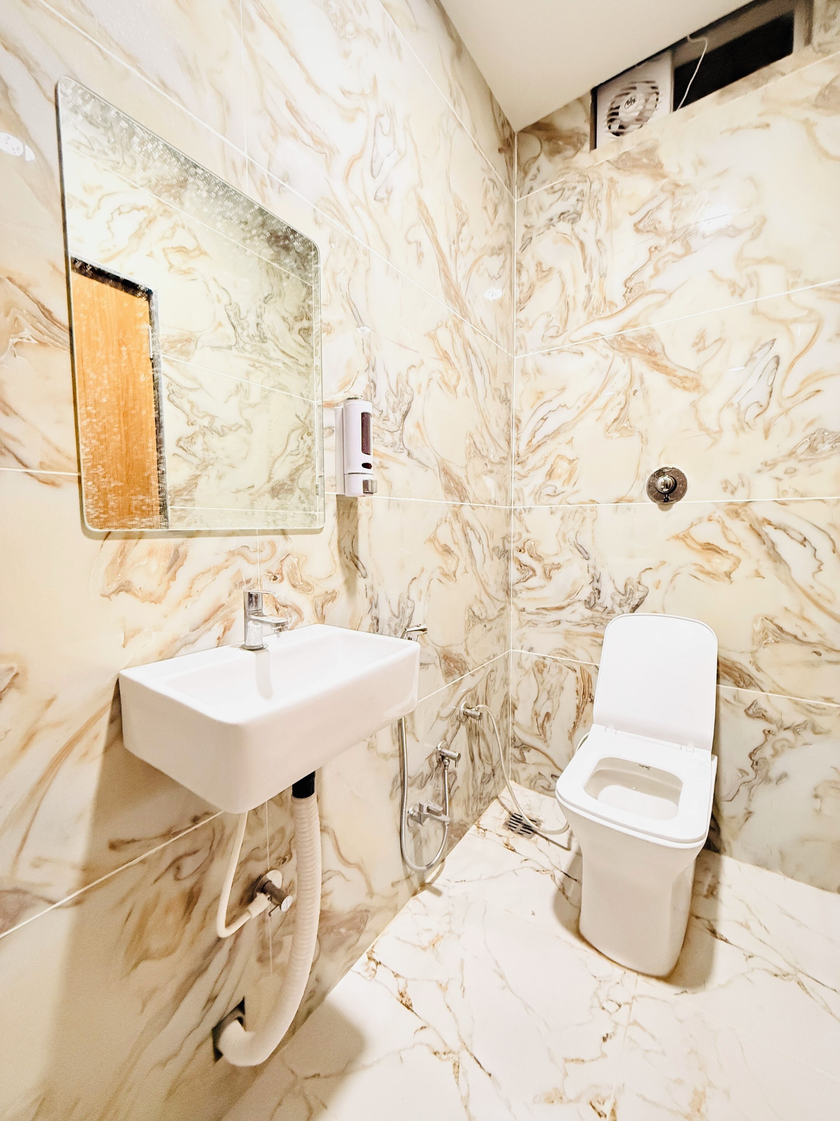 A bathroom with a marble wall, a sink, a toilet, and a mirror.