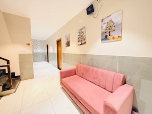 A hotel lobby with a pink sofa, tiled flooring, a staircase, and artwork on the walls. - Hotel Atishay (Ujjain)