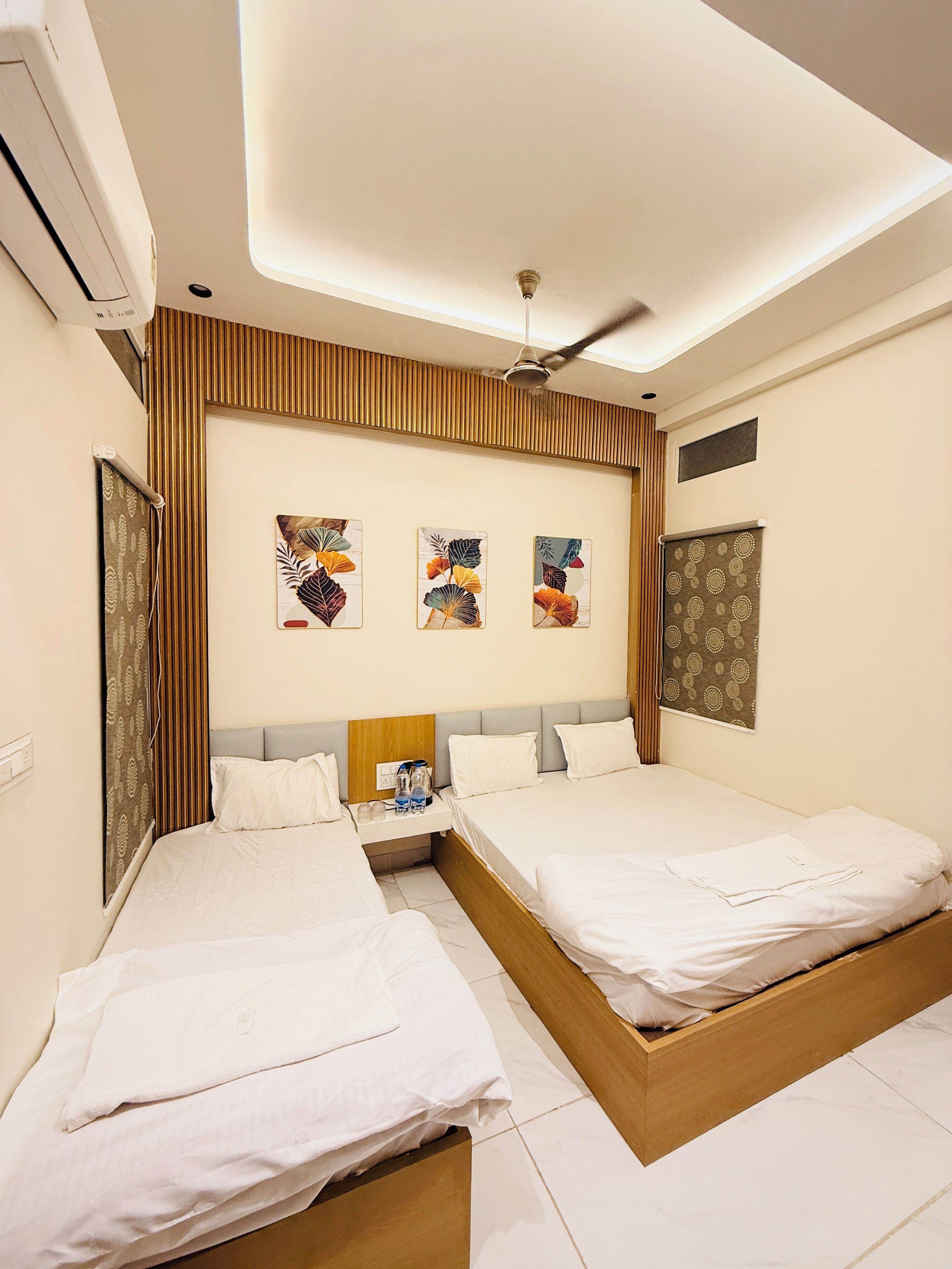 A hotel room with two beds, a ceiling fan, and three wall-mounted artworks.